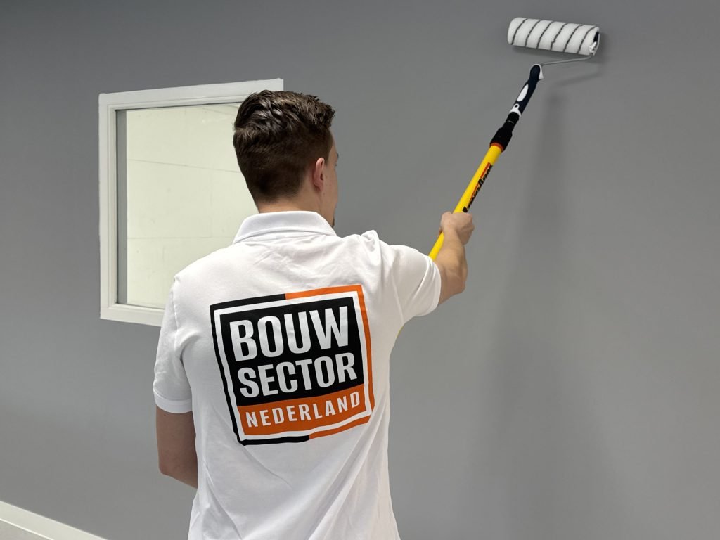 Schilder van Bouwsector Nederland rolt grijze muurverf naast een raam met witte omlijsting