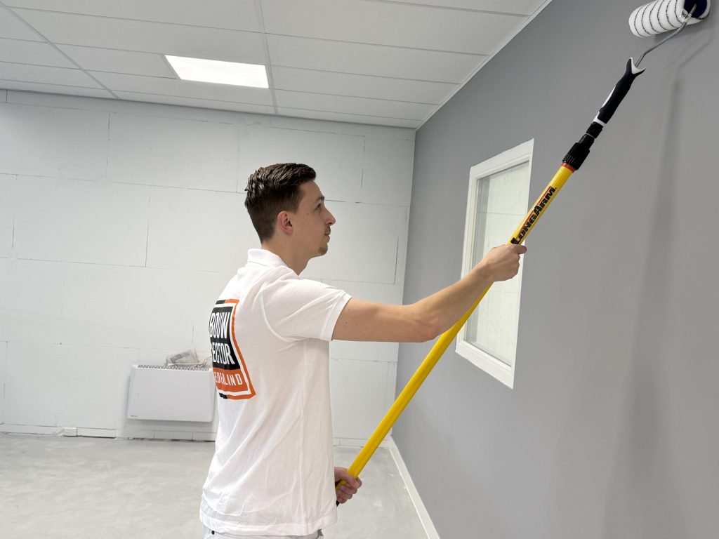 Schilder rolt de bovenkant van een grijze wand vlak onder het plafond