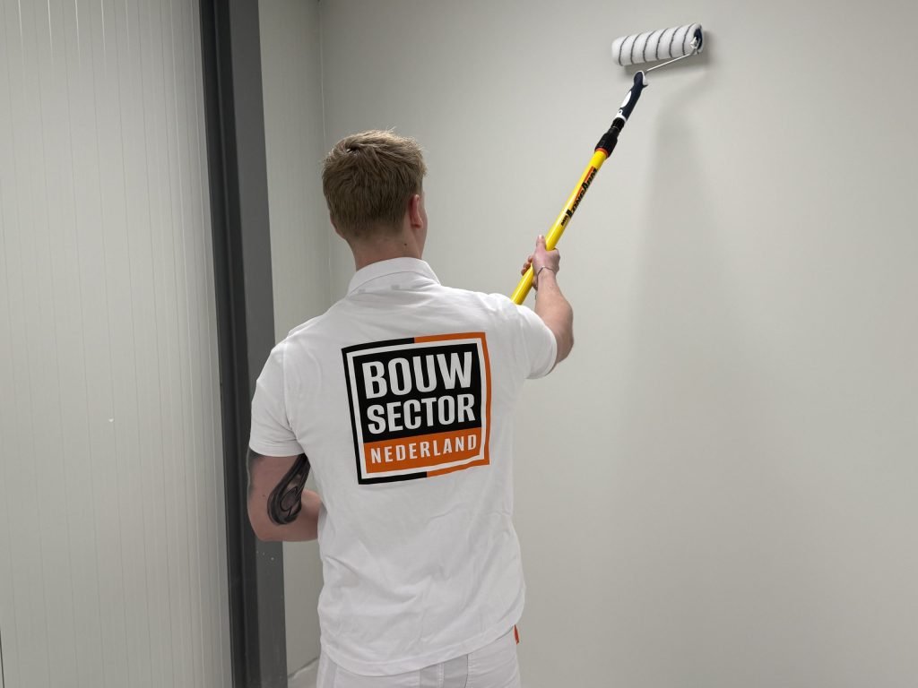Schilder in wit poloshirt rolt een lichte wand in een smalle ruimte