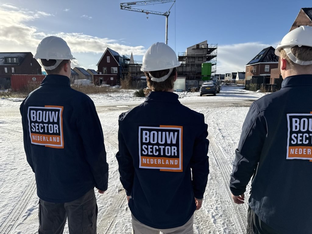 Team van Bouwsector Nederland met helm, van achteren, op een nieuwbouwplek met bakstenen huizen in aanbouw